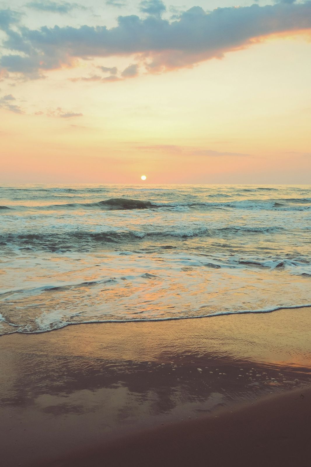 Sunset over the ocean, waves rolling onto the sand
